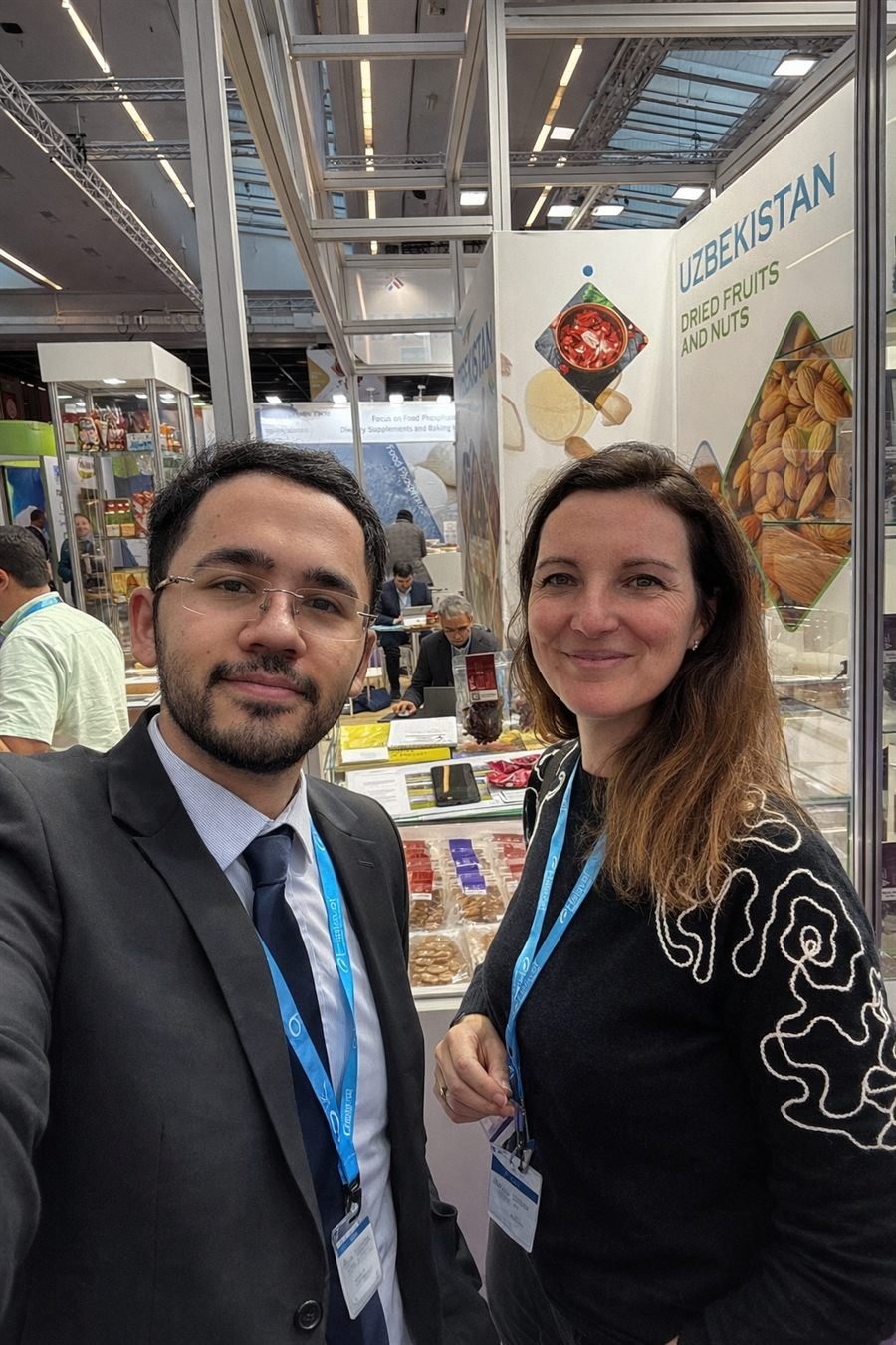 Two people at the Uzbekistan dried fruits and nuts stand at Fi Europe 2025 in Paris, with trays of dried fruit and packed samples laid out on the counter behind them.