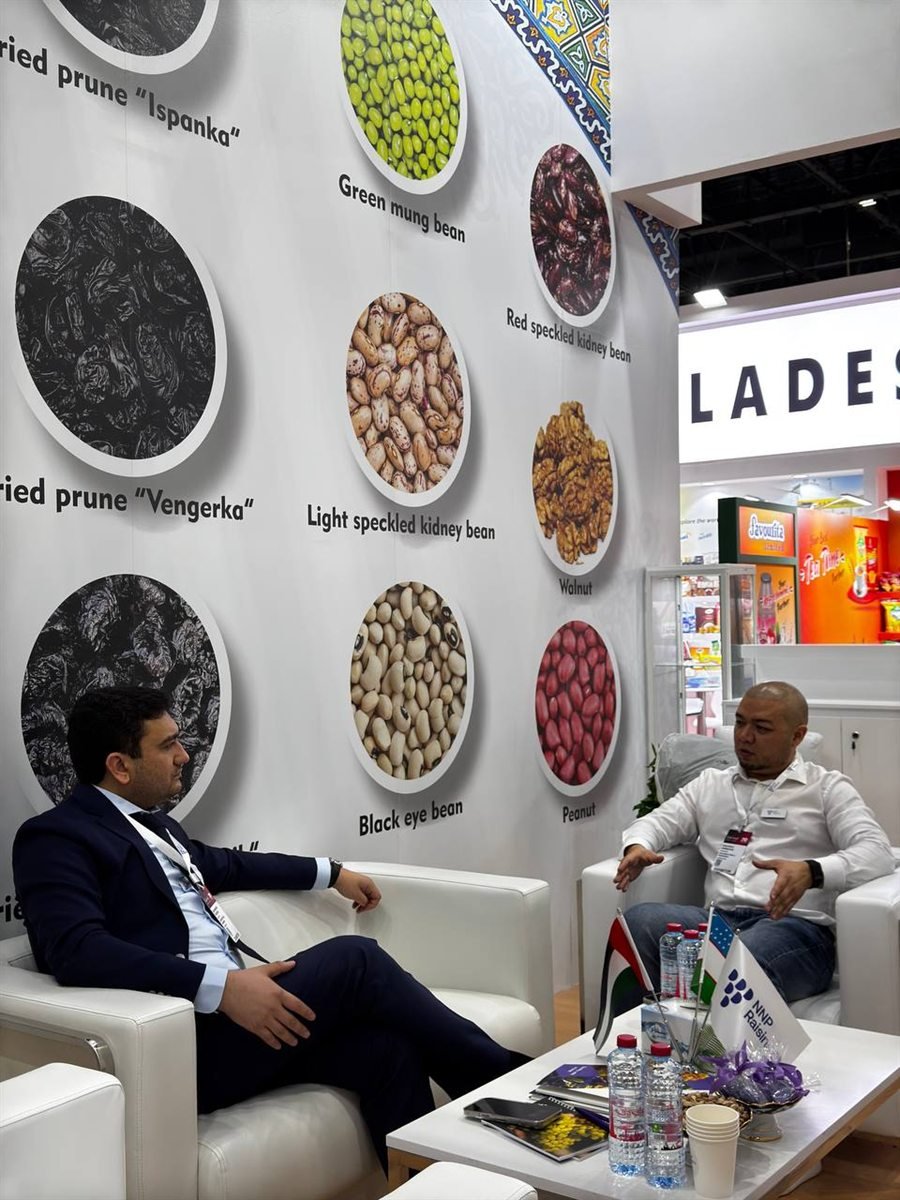 A meeting in the lounge of the NNP Raisins stand at Gulfood 2025, two people seated in armchairs either side of a low table with the NNP Raisins and Uzbek flags on it.