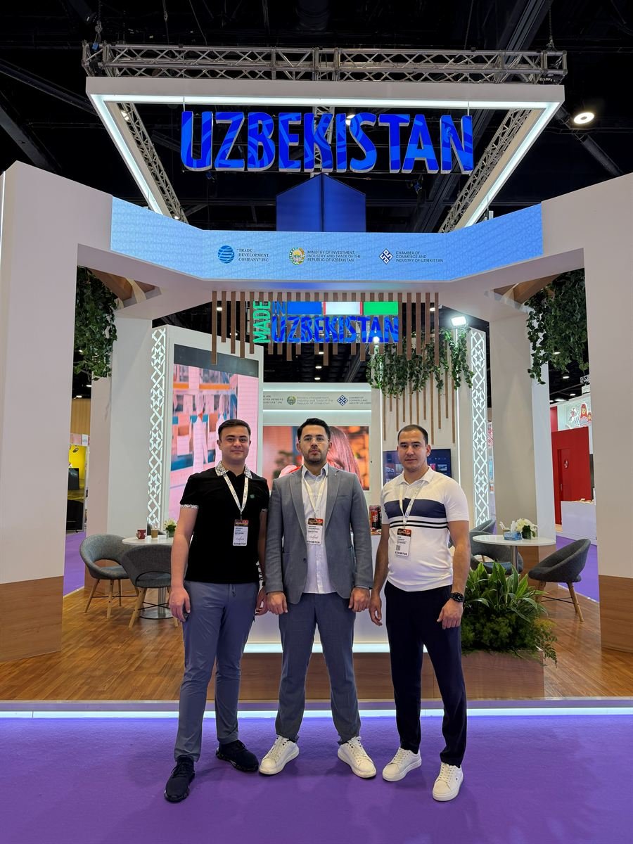 The Uzbekistan national pavilion at Gulfood 2026, its illuminated country sign above the entrance, with three of the NNP Raisins team in front of it.