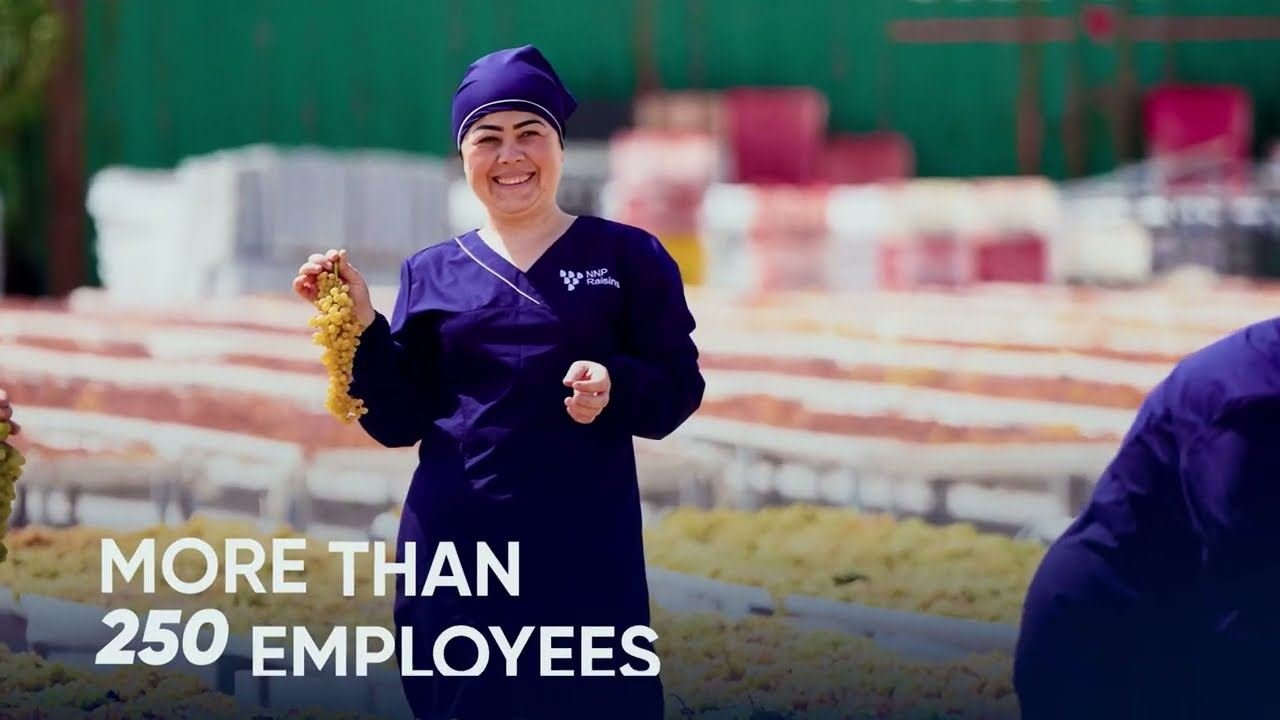 A still from the NNP Raisins company film: a worker holding grapes at the drying yard.